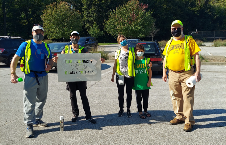 Volunteers wearing masks and yellow vests hold stencils and spray paint for a storm water stenciling event.